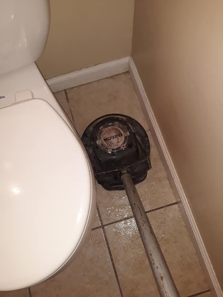 Toilet plunging tool on bathroom tile floor beside a toilet