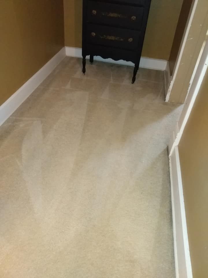 Narrow carpeted hallway with beige walls and a dark dresser at the end