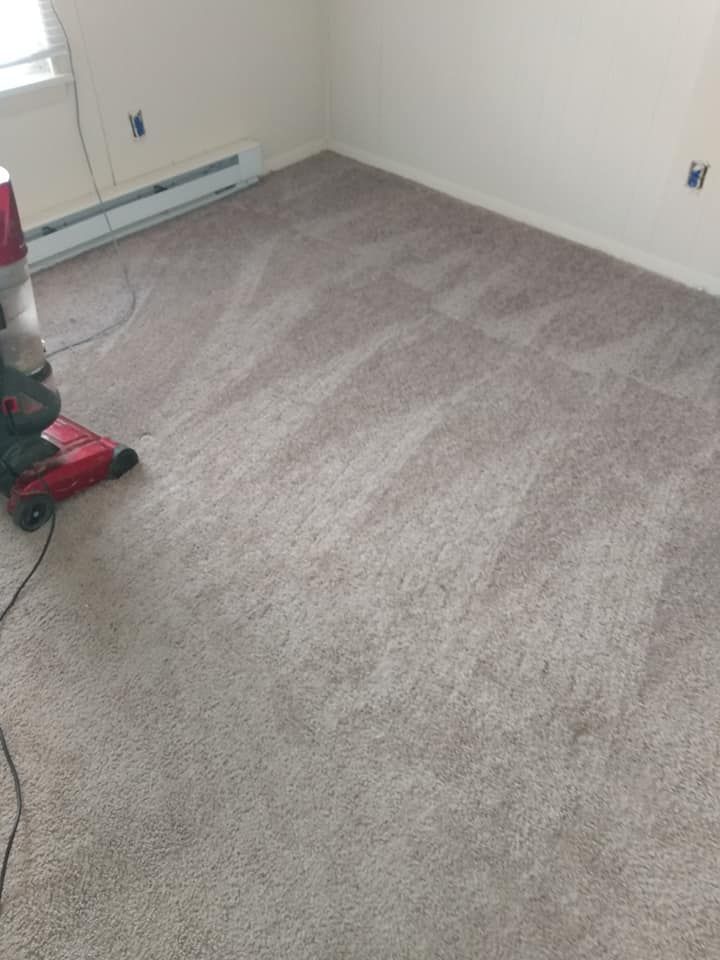 Vacuum cleaning a beige carpet in an empty room with white walls.