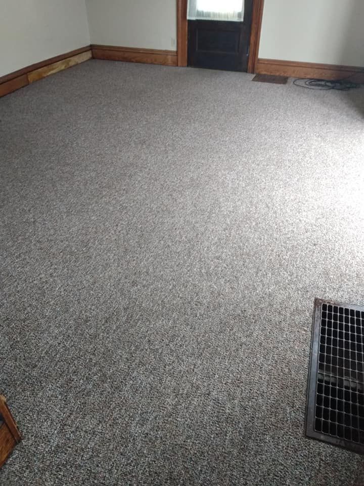 Empty carpeted room with gray speckled flooring, wood trim, and a floor vent