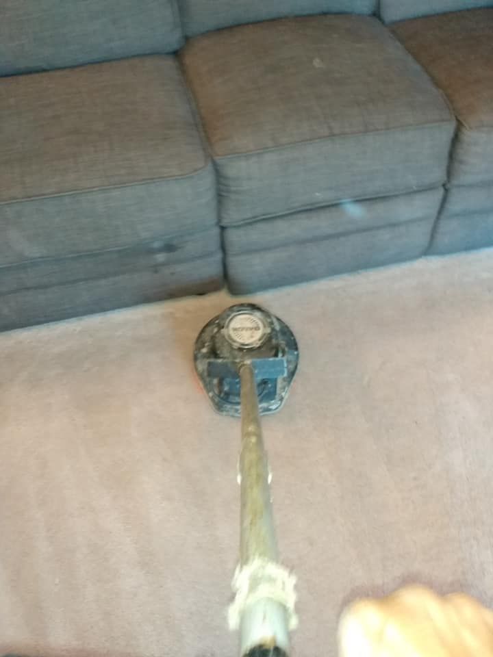 Handheld vacuum nozzle on a light blanket in front of a gray sofa