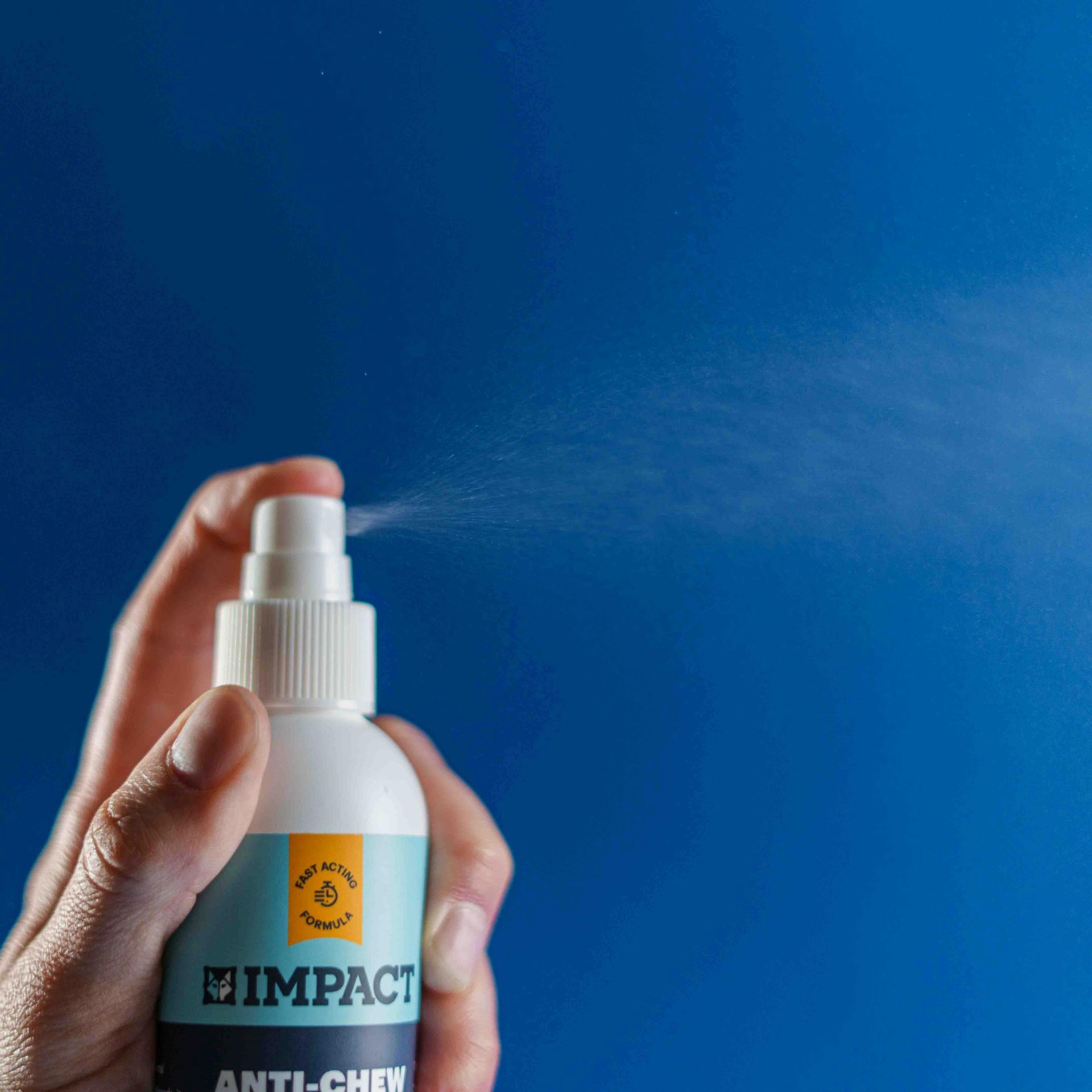 Hand holding a white spray bottle labeled “IMPACT” against a blue background