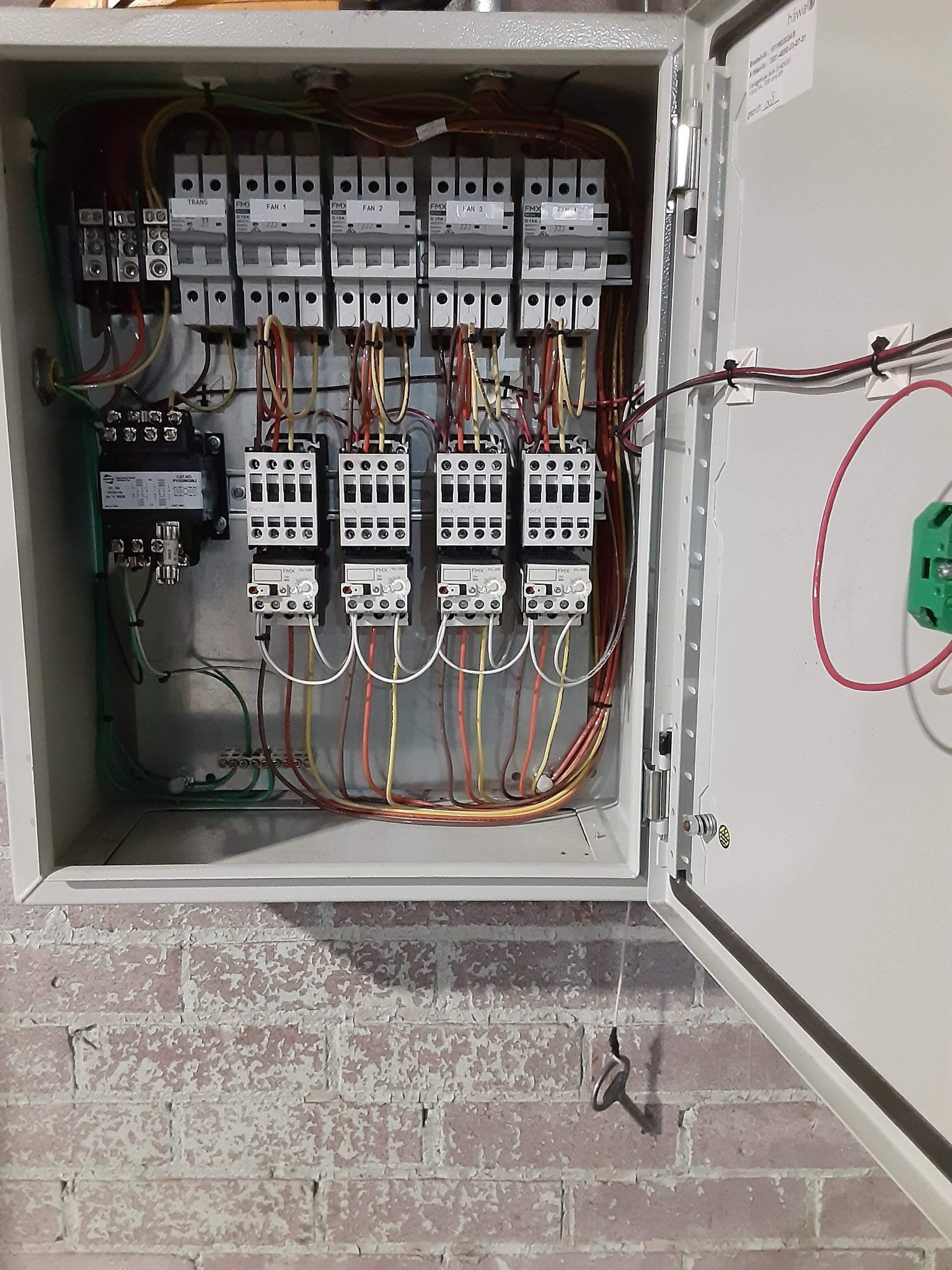 A electrical box with a lot of wires coming out of it is sitting on a brick wall.