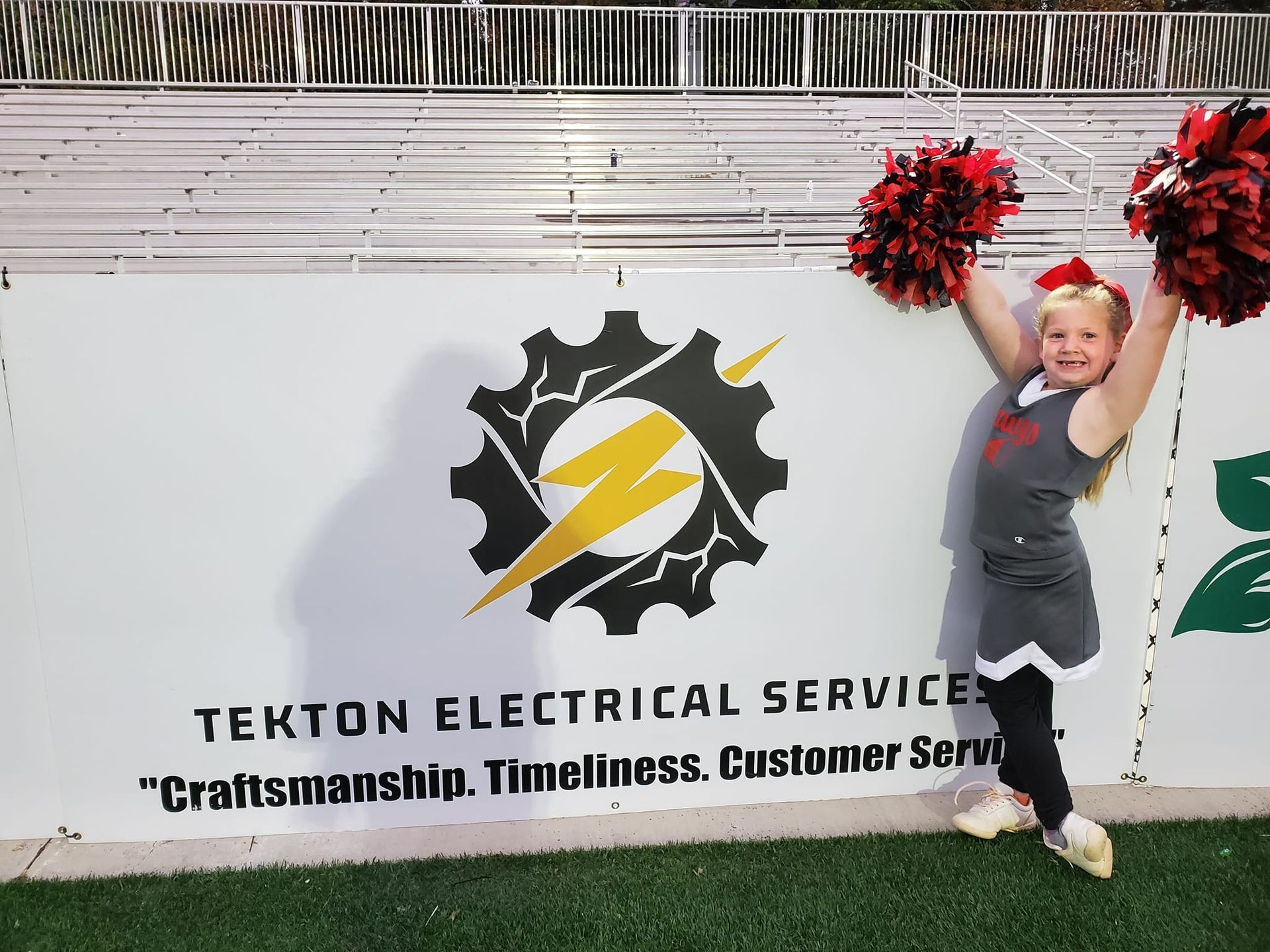 A cheerleader stands in front of a sign for tekton electrical services