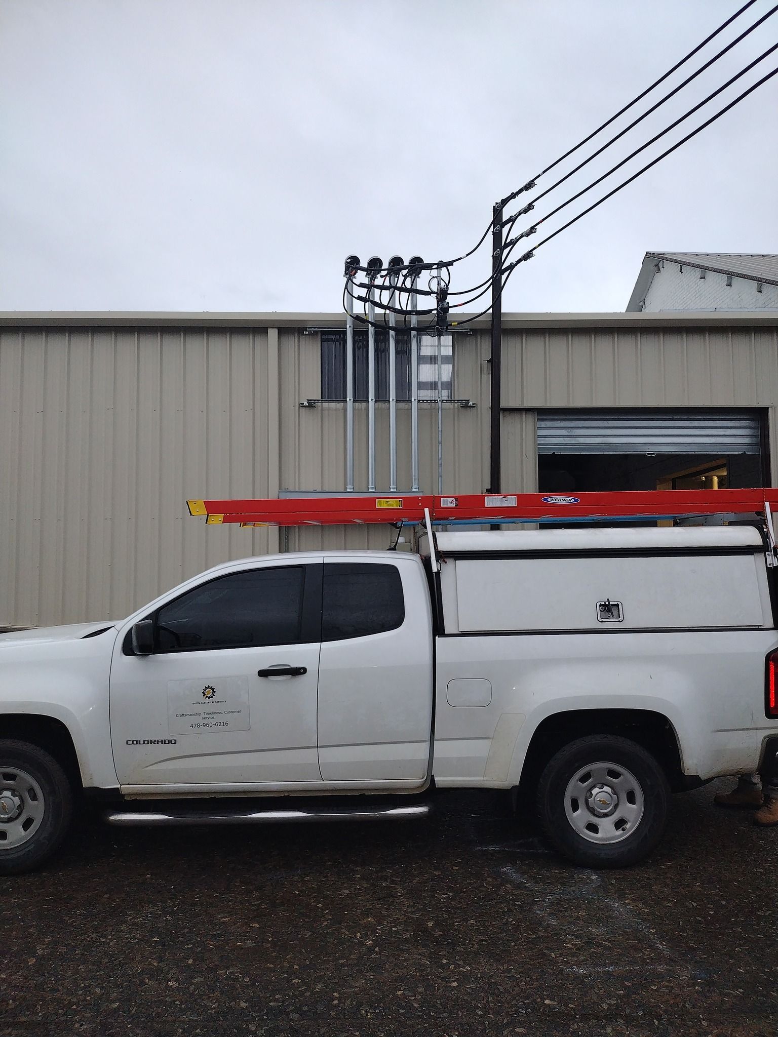 A white truck with a ladder on top of it is parked in front of a building.