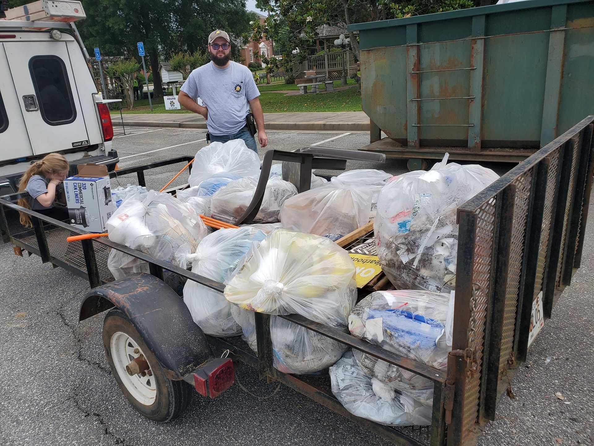 A man is standing next to a trailer filled with bags of trash.