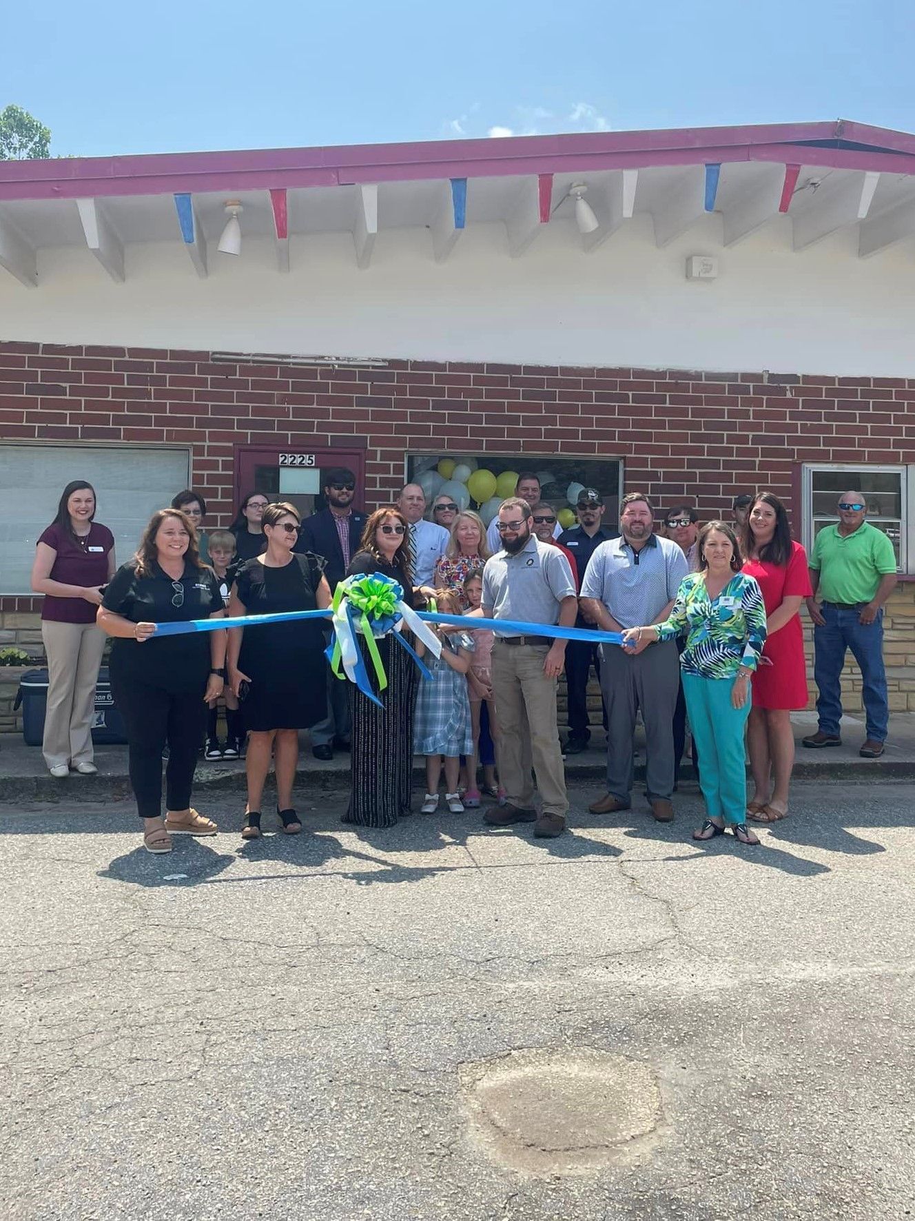 A group of people are cutting a blue ribbon in front of a brick building.