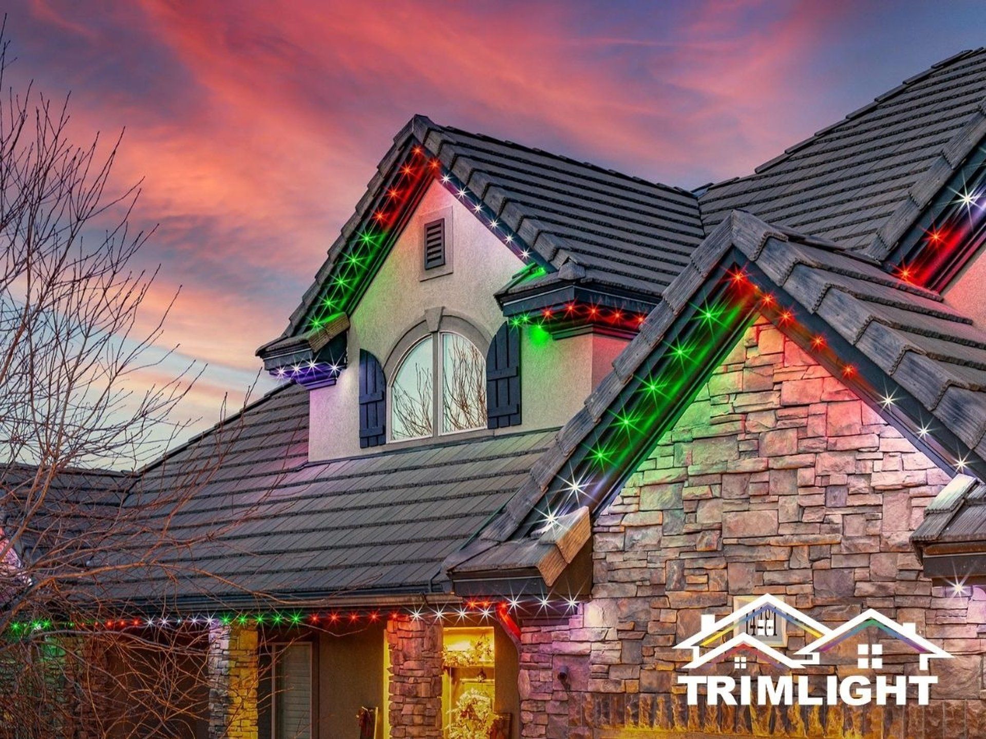 House with Christmas lights along the roofline, red, green, and white against a sunset.