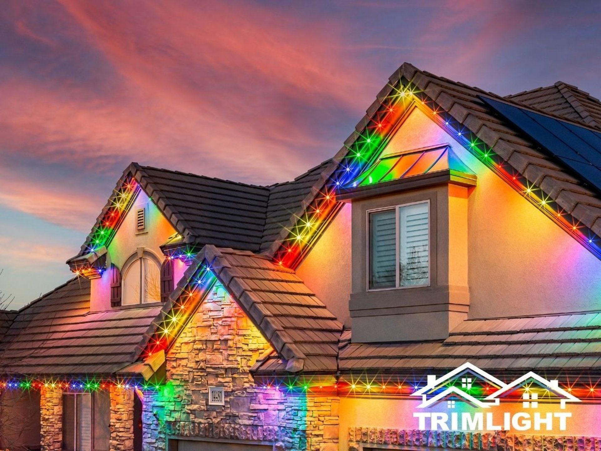 House with colorful LED lights along the roofline against a sunset sky.