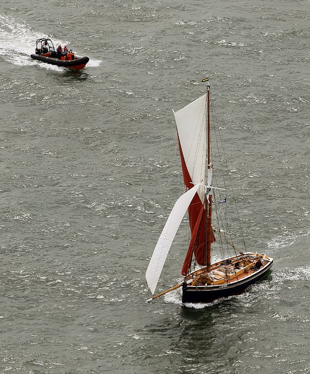 A boat with a white sail is floating in the water next to another boat