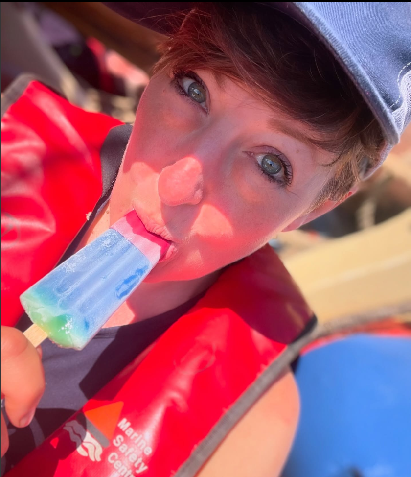 A person wearing a life vest is eating a popsicle