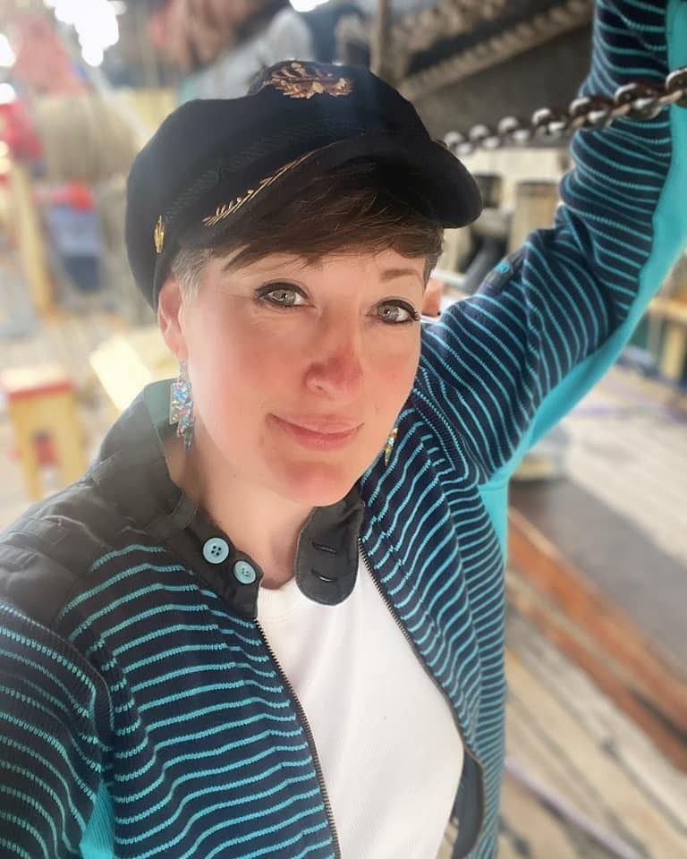 A woman wearing a hat and a striped jacket is taking a selfie.
