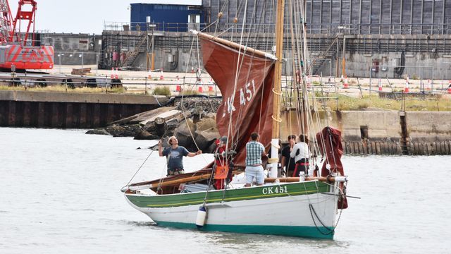 A boat with a red sail is floating on top of a body of water.
