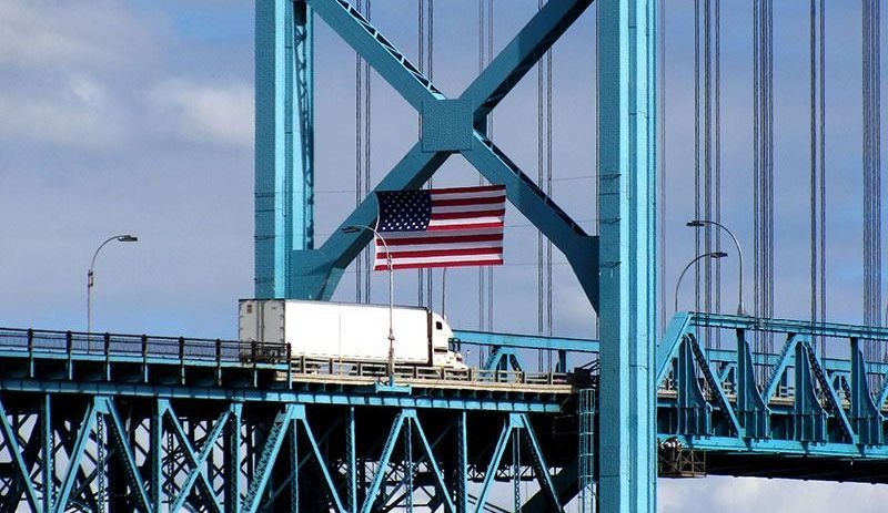 A truck is driving over a bridge with an american flag hanging from it