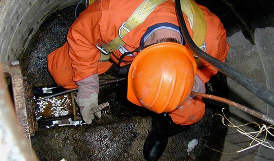Construction guy in manhole wearing orange jumpsuit fixing sewer line 