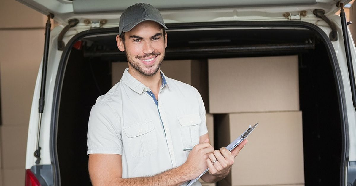 A delivery man is standing in front of a van holding a clipboard.