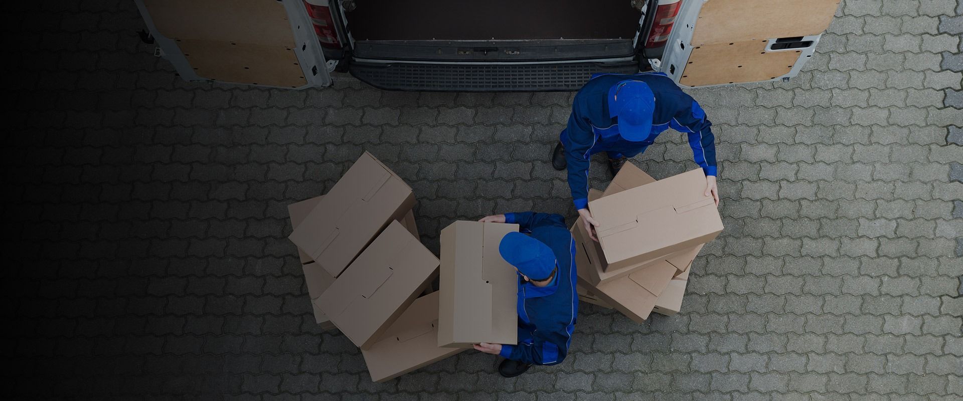 An aerial view of two delivery men carrying boxes out of a truck.