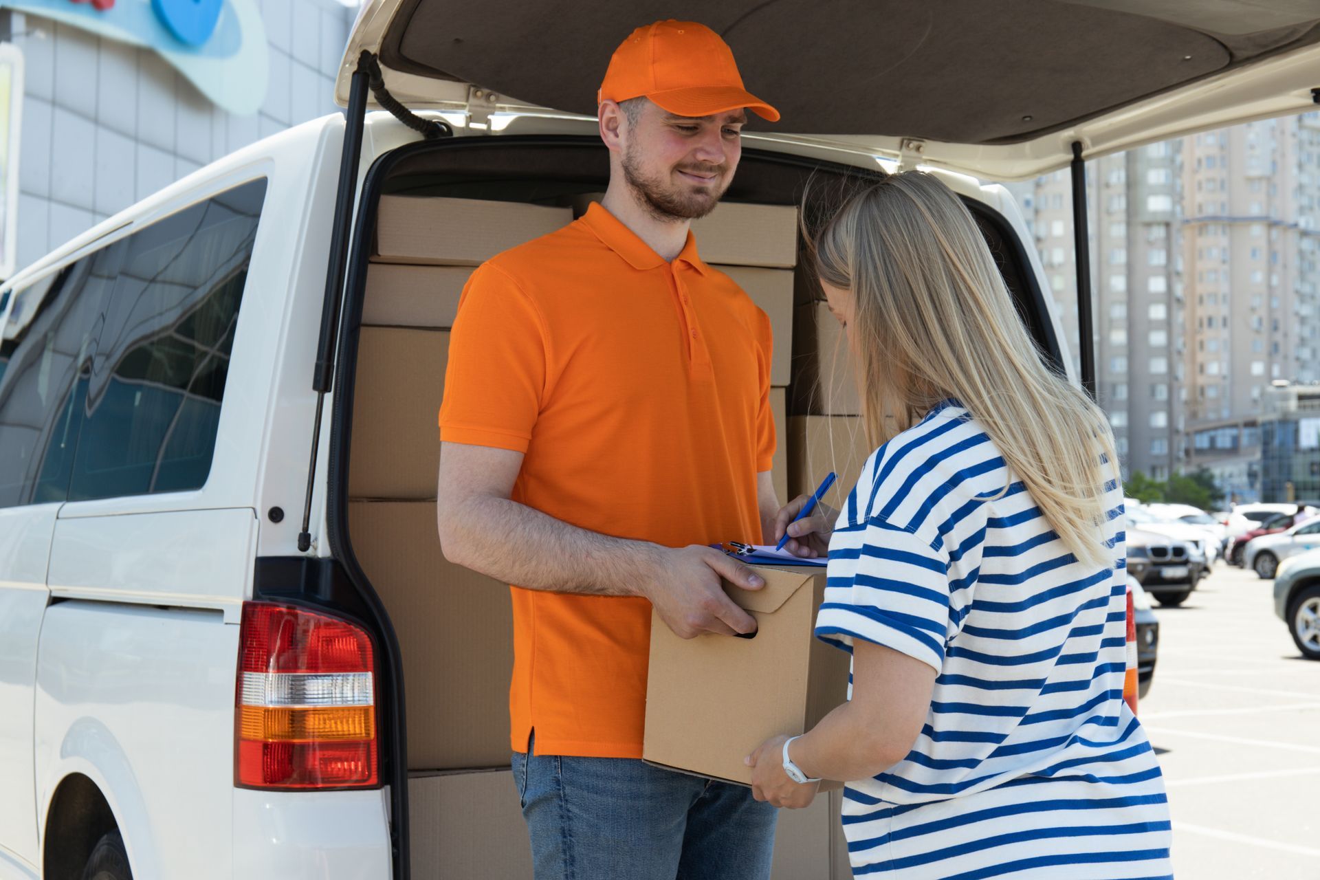 Delivery person hands a package to a woman at a van. They are outdoors.