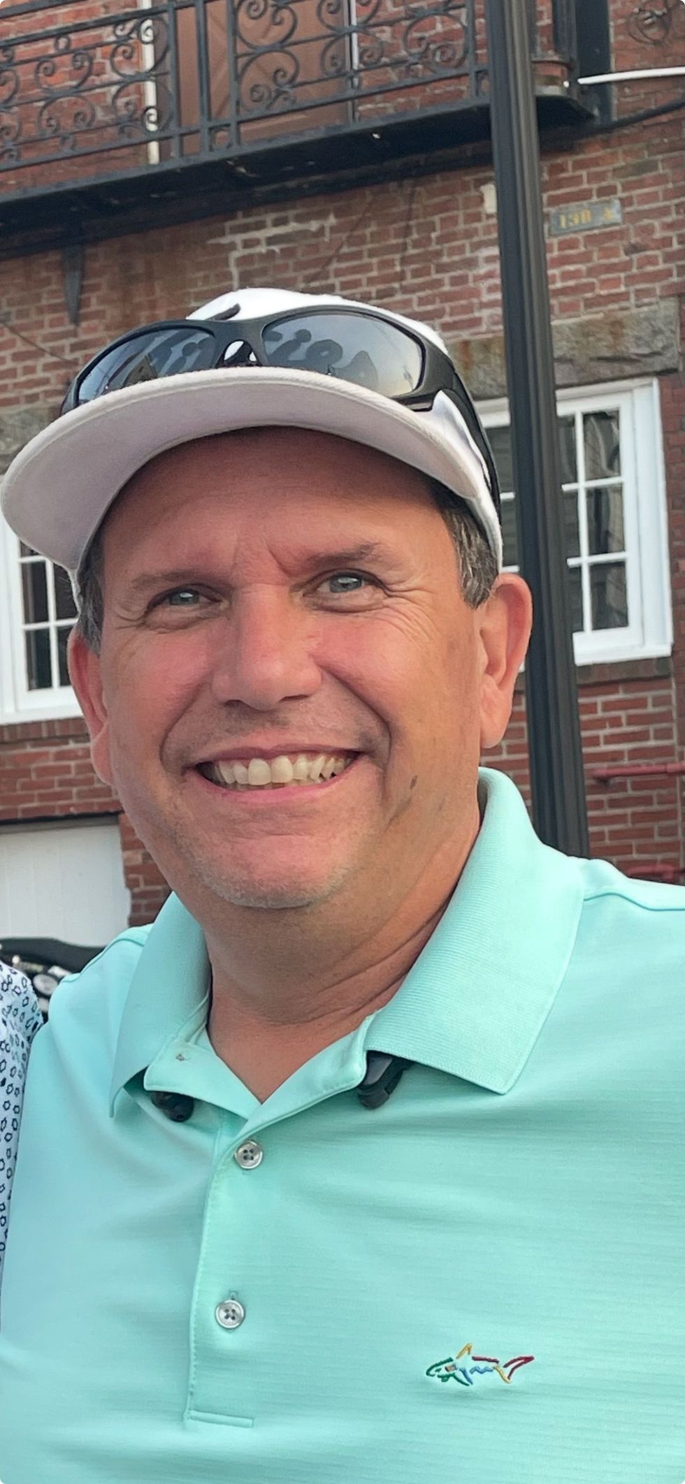 Smiling Black man with arms crossed, wearing a blue hard hat, white shirt, and tie outdoors.