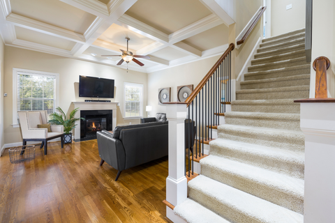 Living room with fireplace, stairs, and a dark gray sofa. Brown wood flooring and coffered ceiling.