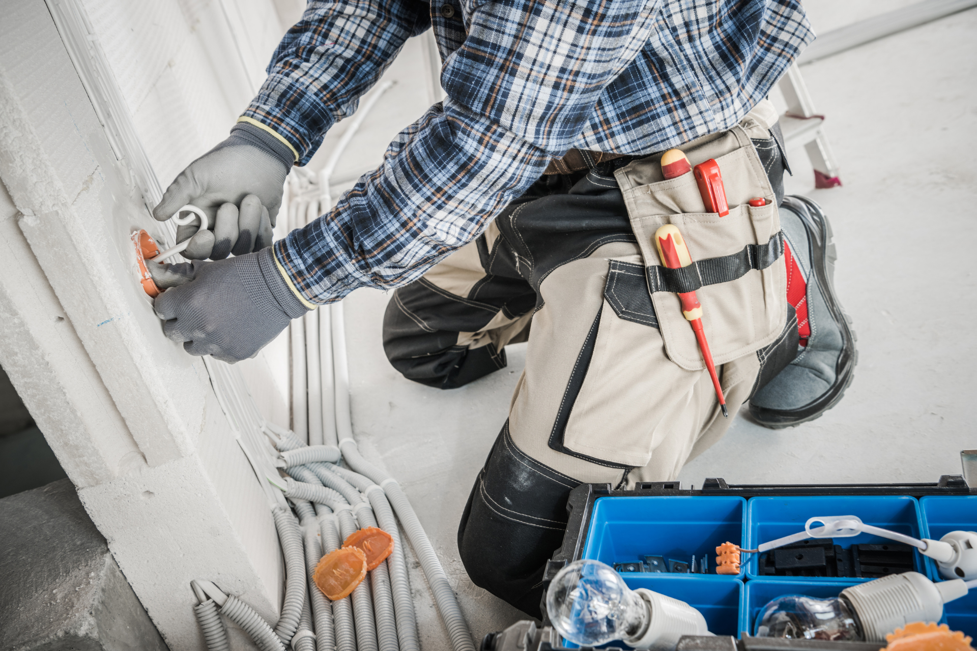 Electrician working with wires, wearing a plaid shirt and tool belt.
