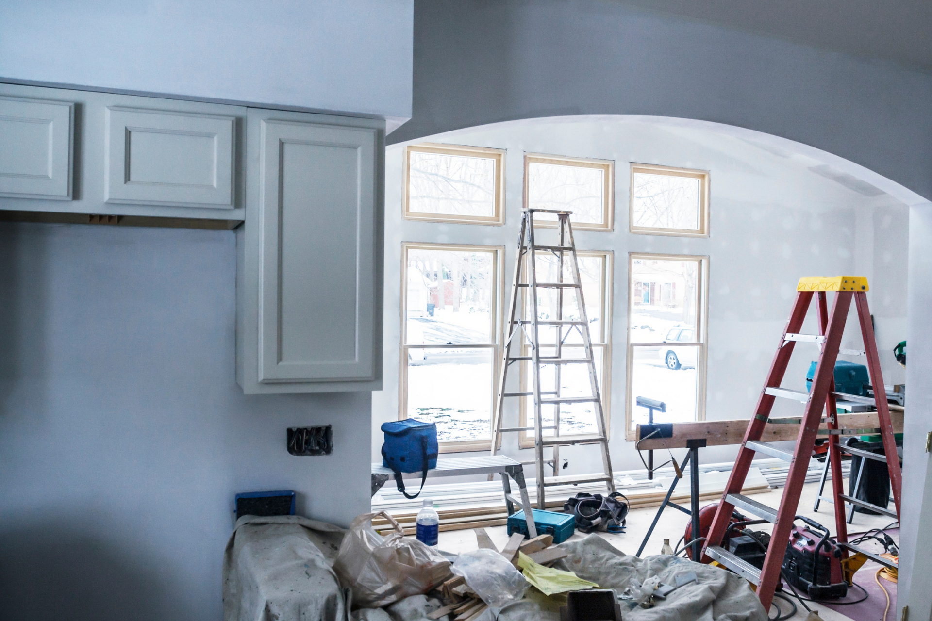 Kitchen under construction with cabinets, windows, and ladders.