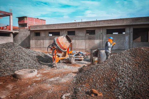 Construction worker near concrete mixer and piles of gravel at a building site under a blue sky.