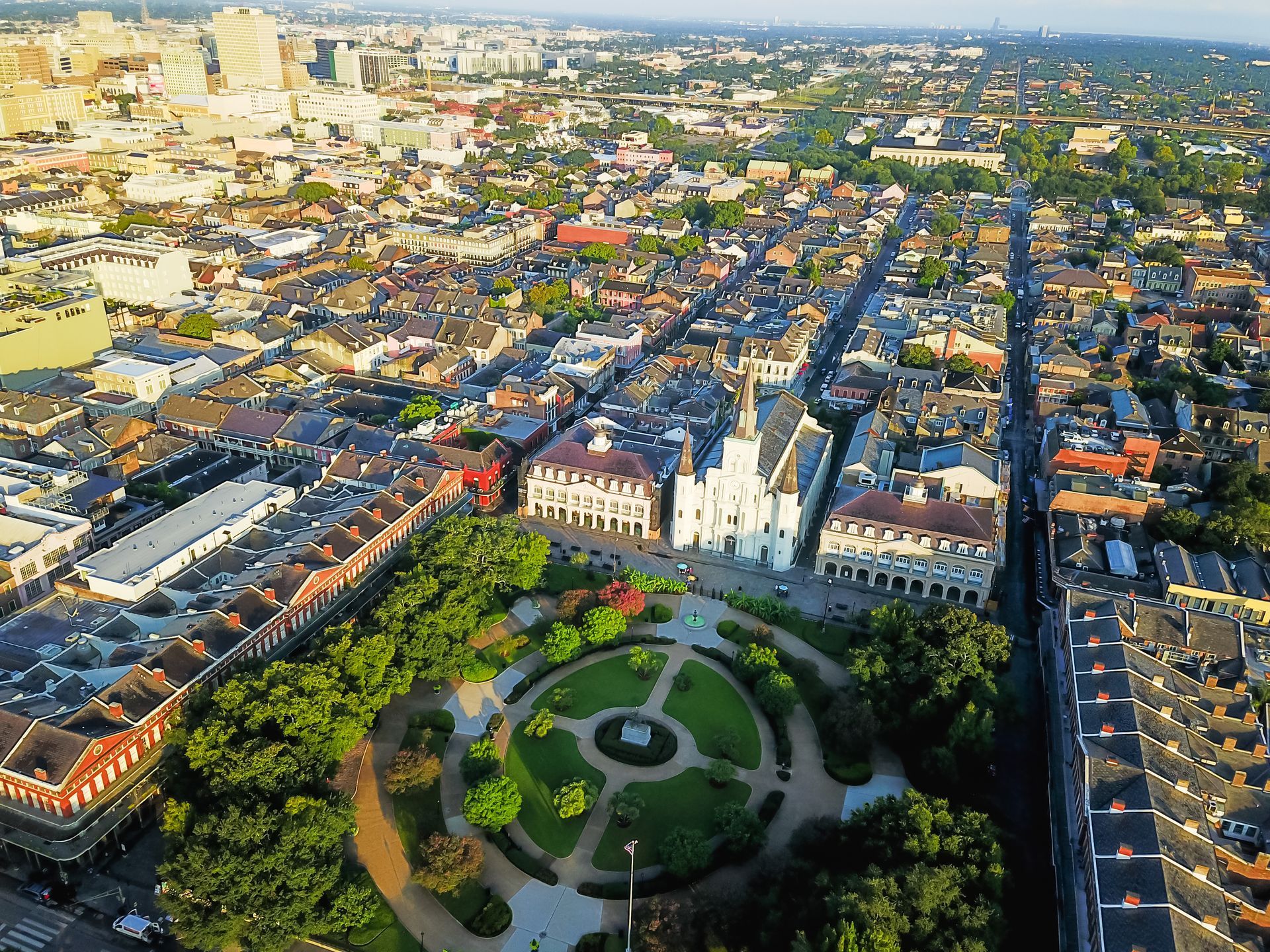 Aerial view of a city with a landscaped circular park at the center, surrounded by dense buildings in warm sunlight