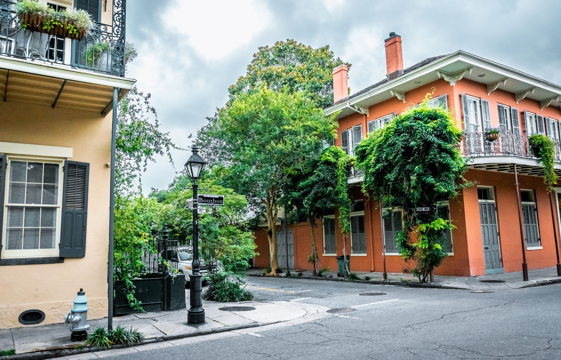 Quiet street corner with orange and cream buildings, balconies, trees, and a cloudy sky.