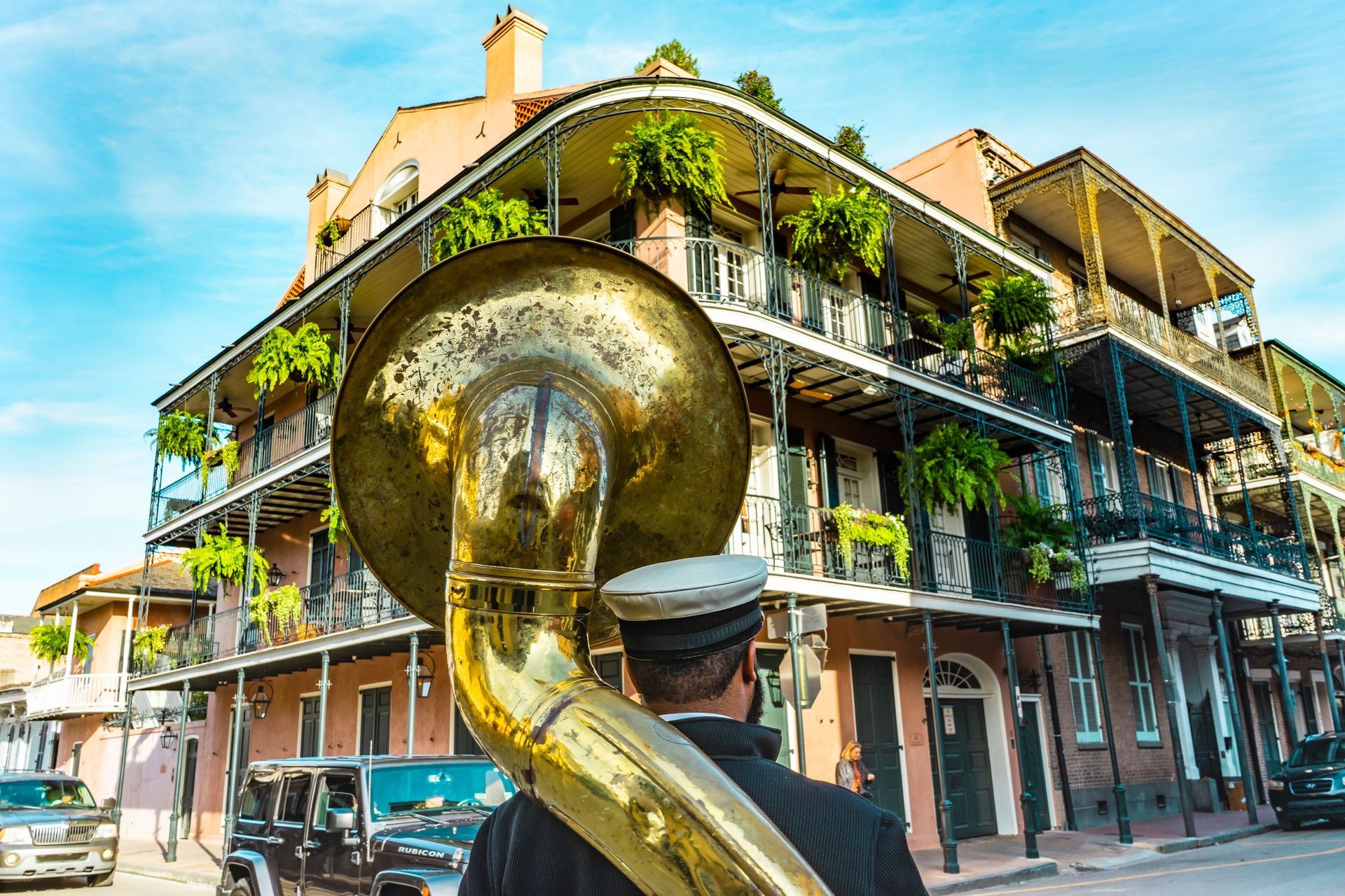 Street musician playing sousaphone in front of a colorful New Orleans-style balcony building
