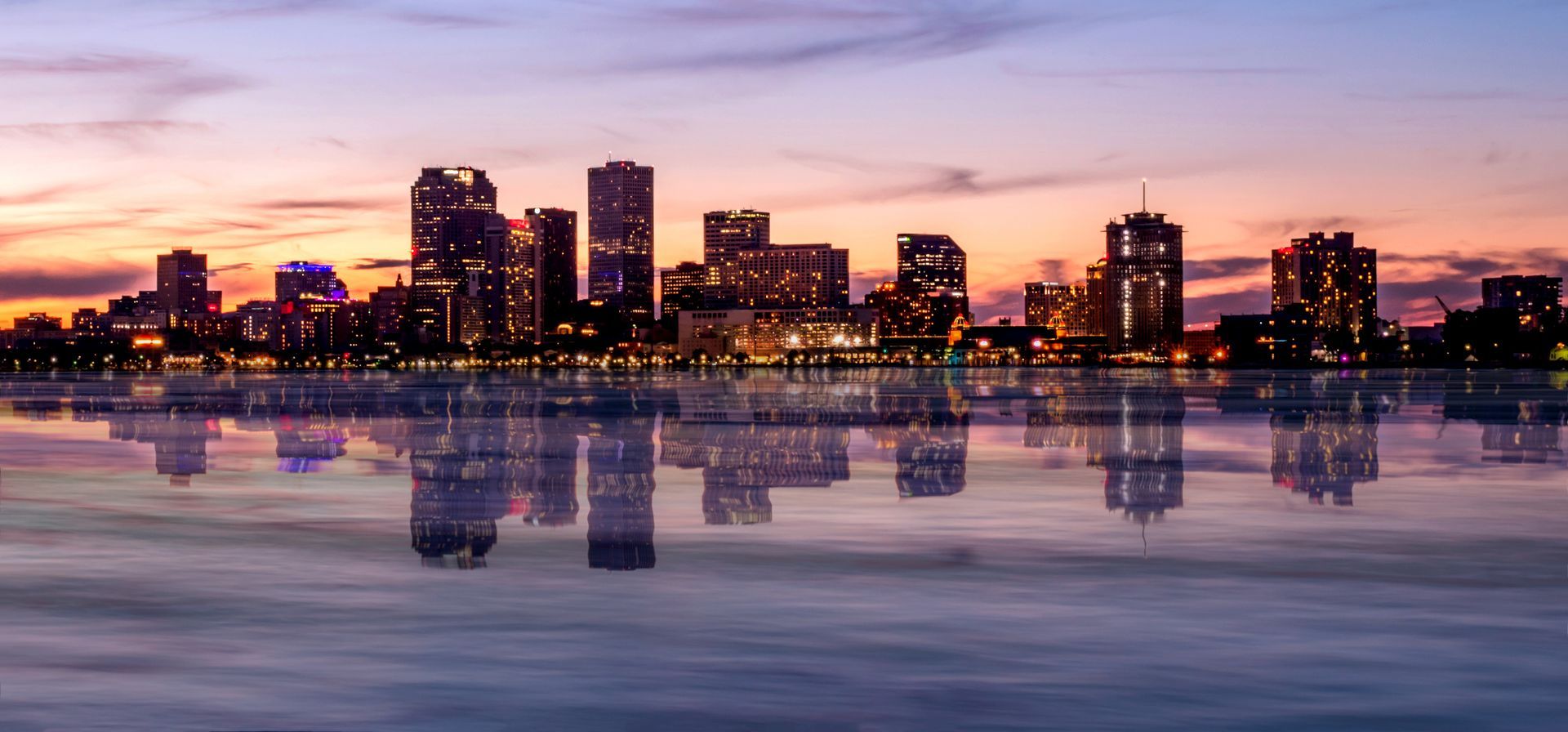 City skyline at sunset reflected in calm water with purple and pink skies