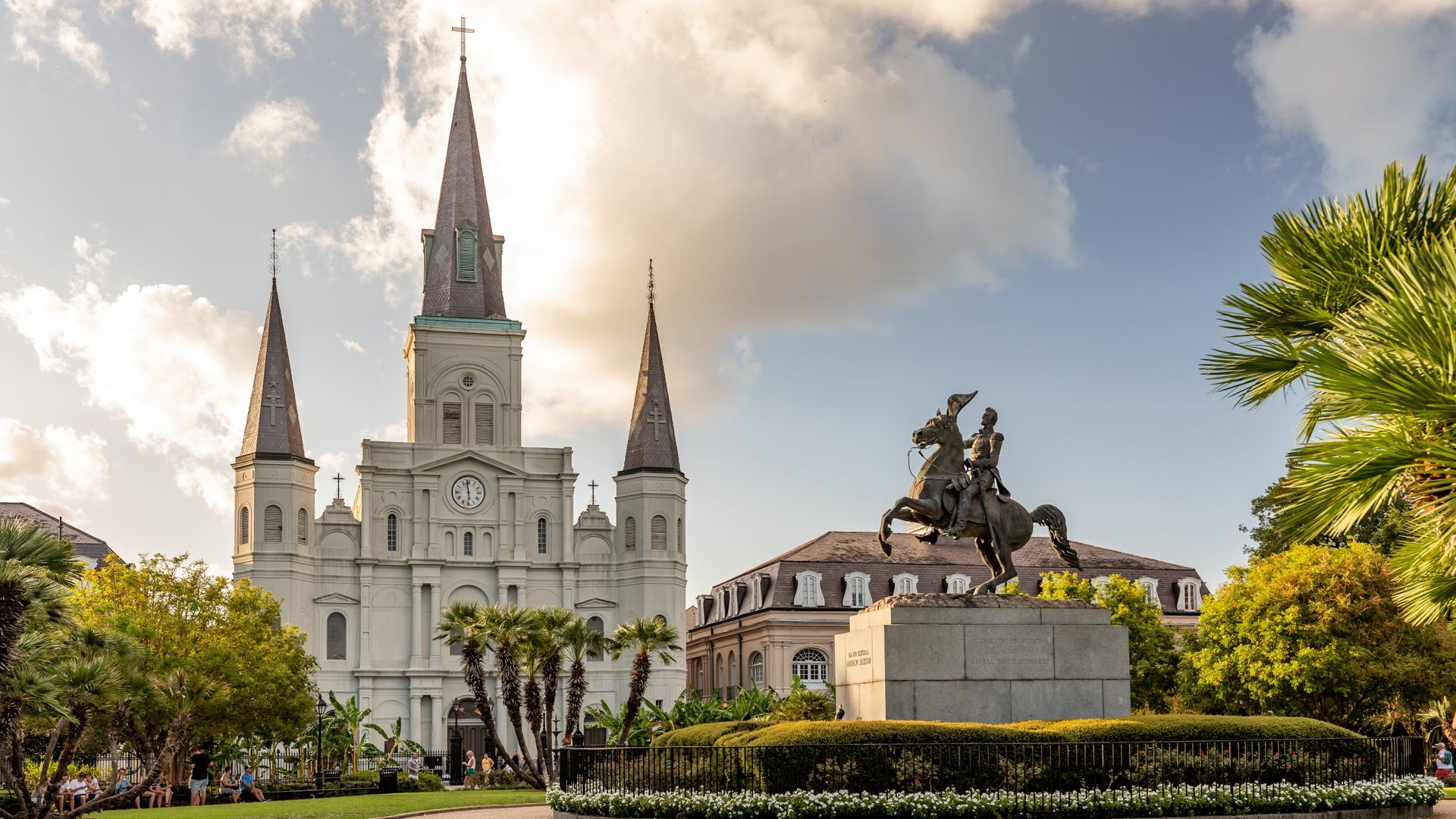 White cathedral with spires beside equestrian statue and palm trees in a sunny plaza