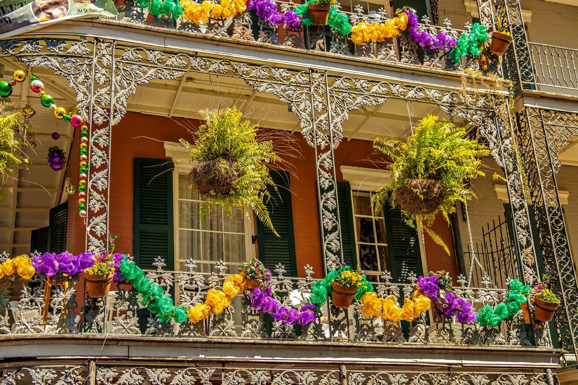Balcony with ornate white ironwork, hanging green plants, and colorful purple, green, and yellow flower garlands
