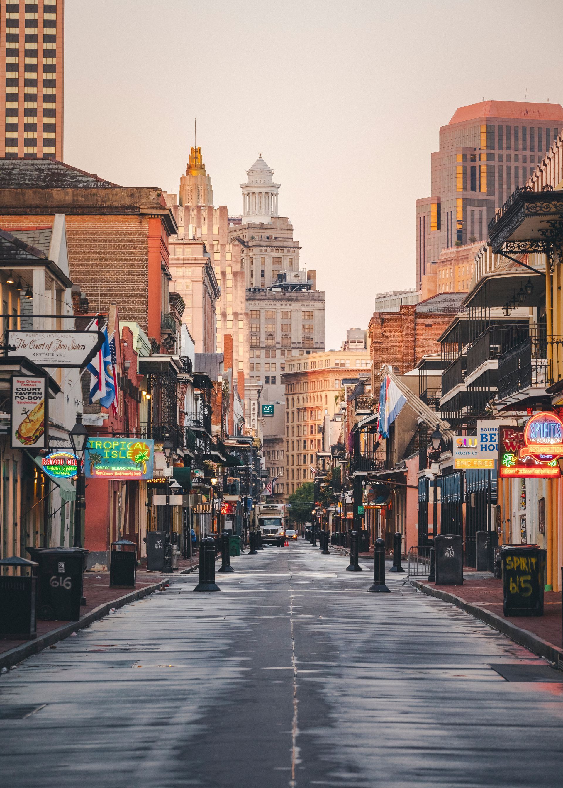 Rain-soaked empty city street lined with lit storefronts and tall historic buildings at dusk