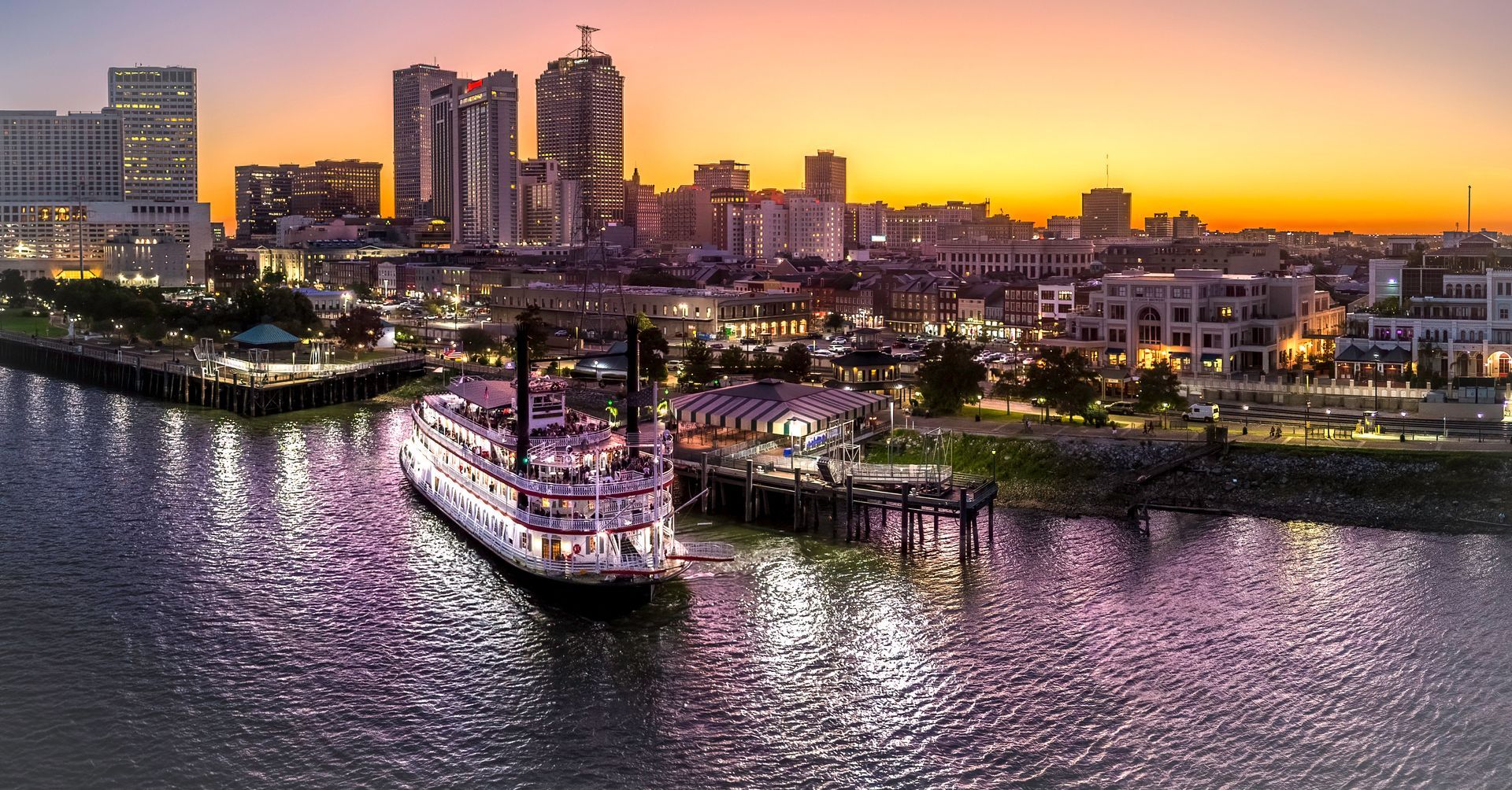 Sunset harbor skyline with a lit ferry on calm water and city buildings glowing in the background