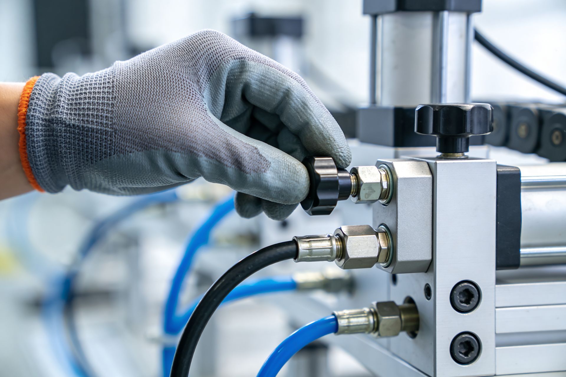 A gloved hand adjusts a knob on industrial pneumatic equipment with blue hoses. A gloved hand adjusts a knob on industrial pneumatic equipment with blue hoses.