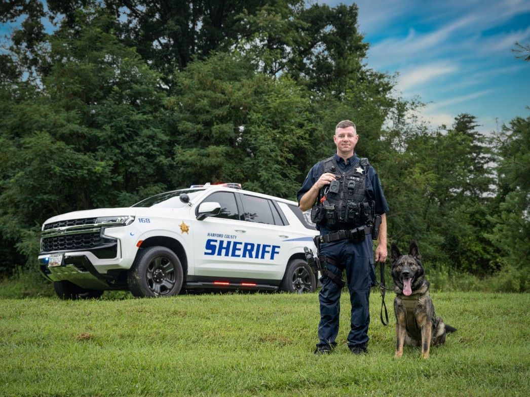 A police officer and his dog are posing for a picture in front of a sheriff 's car.