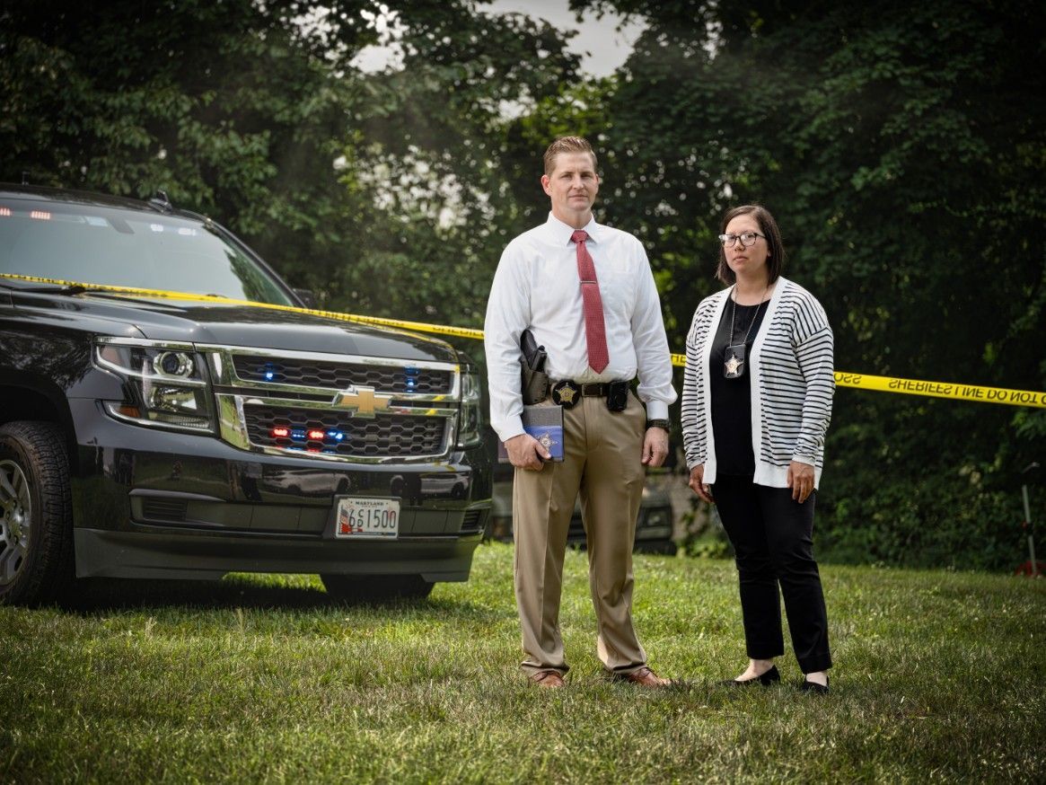 A man and a woman are standing in front of a police car.