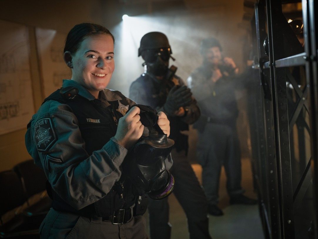 A woman in a military uniform is holding a helmet in a dark room.