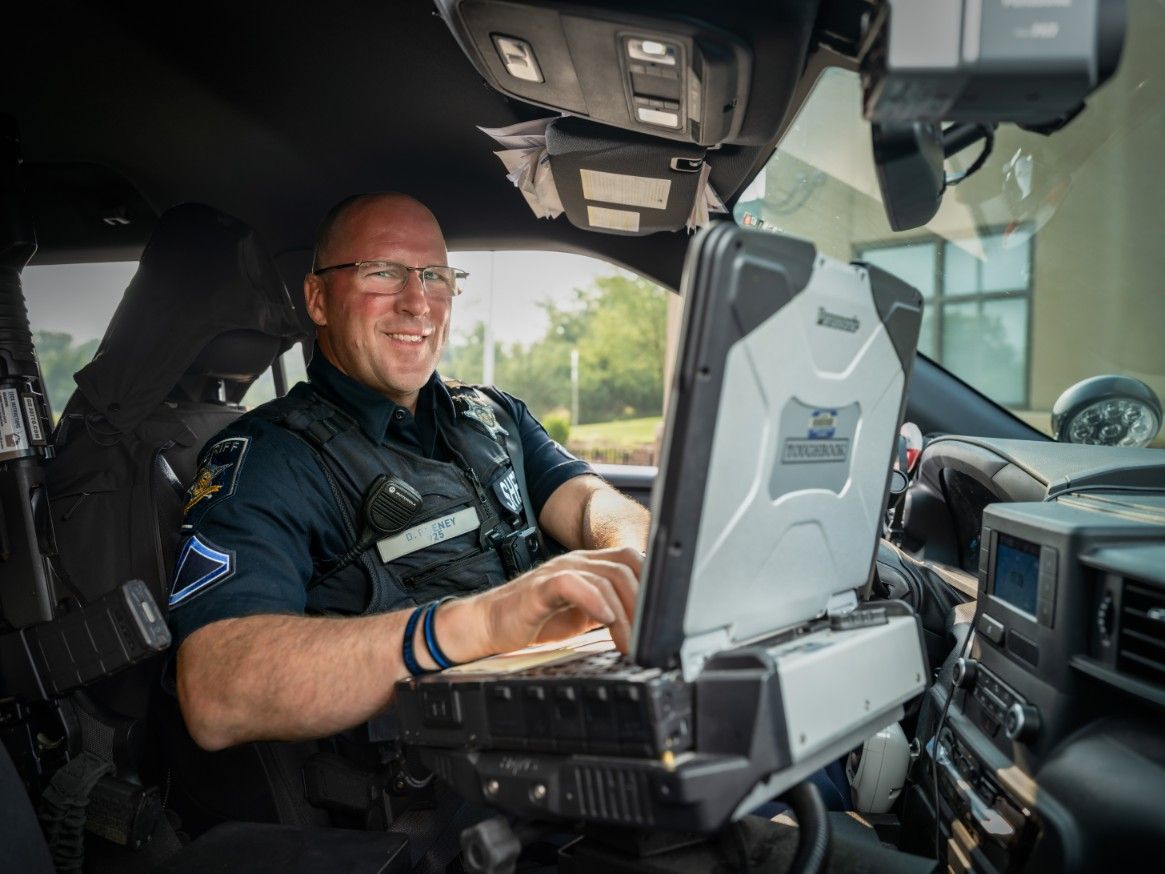 A police officer is sitting in a car using a laptop computer.
