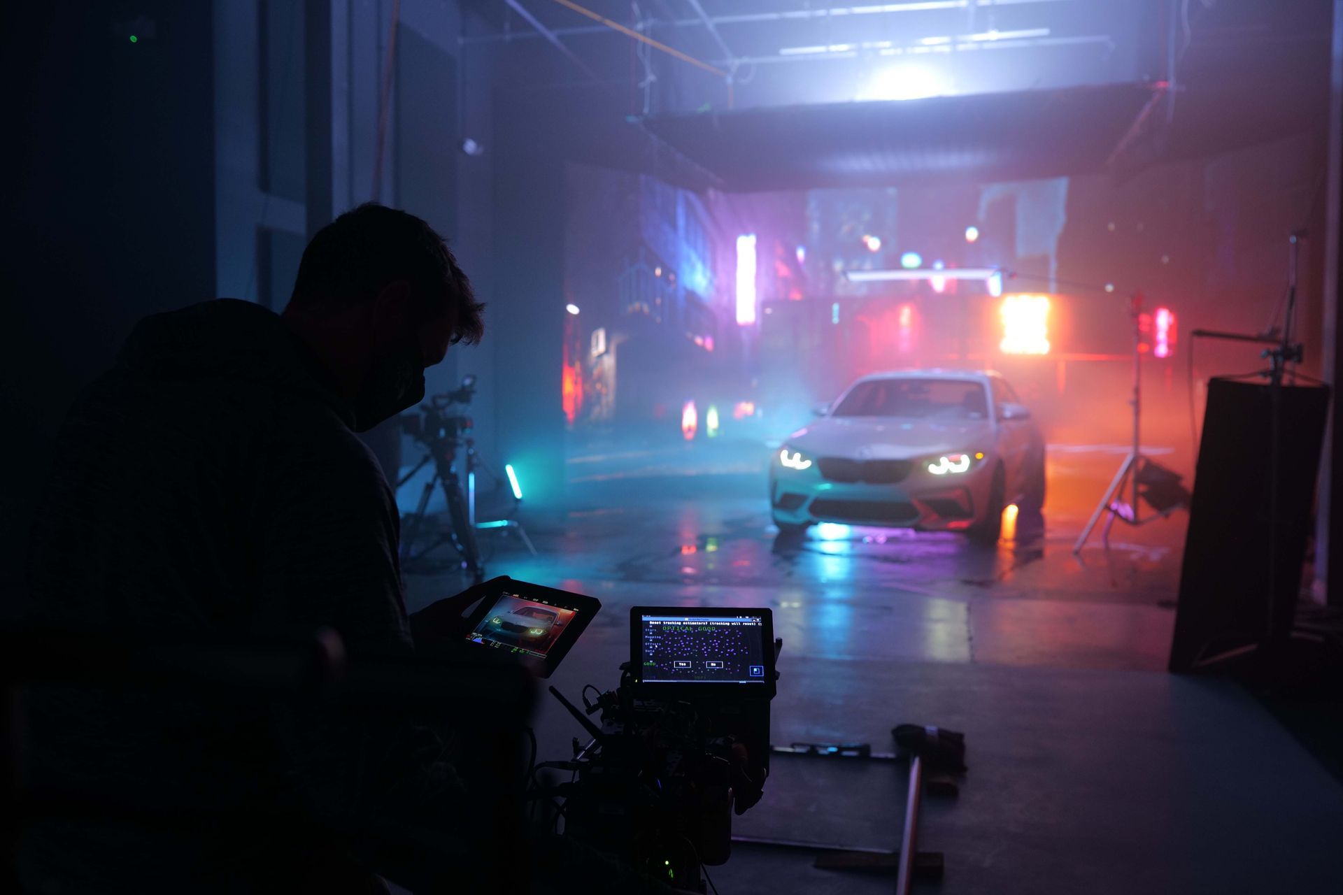 A man is holding a cinema camera in front of a car in a virtual production studio.