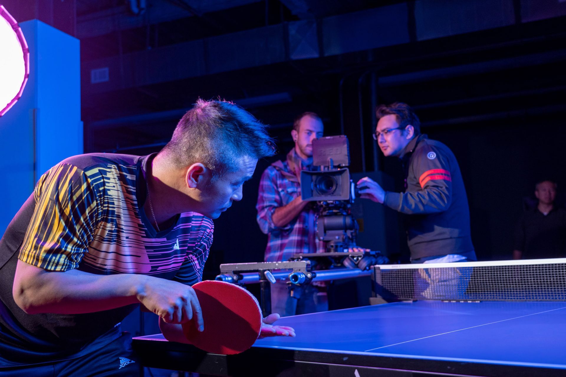 A man is playing ping pong with a cameraman behind him.