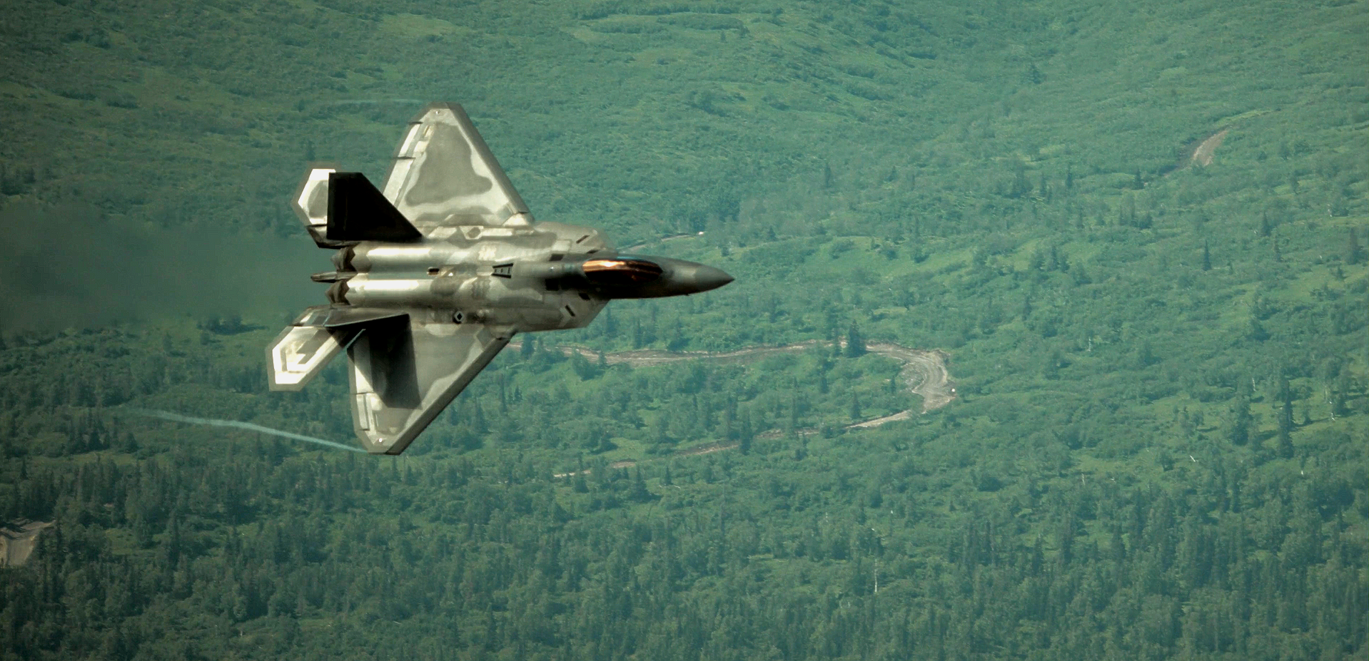 A fighter jet is flying over a forest.