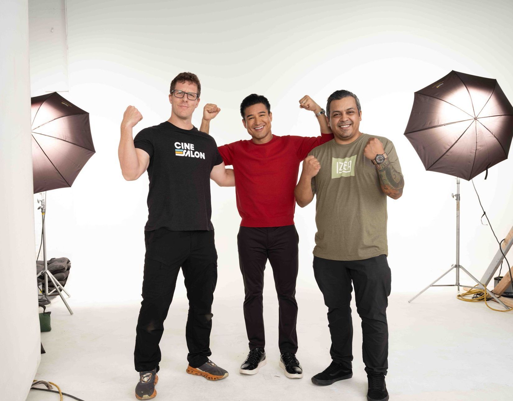 Three men in a studio setting, flexing arms. One in black shirt, one in red, one in green, with white backdrop.
