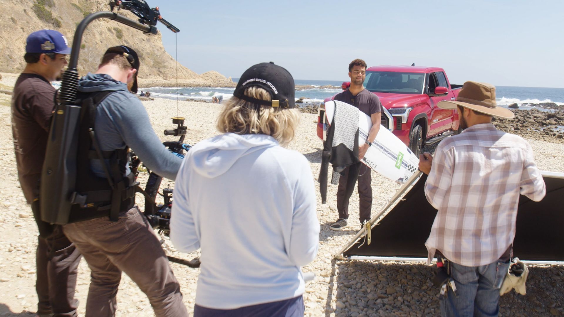 A group of people are standing on a beach with a red truck in the background.
