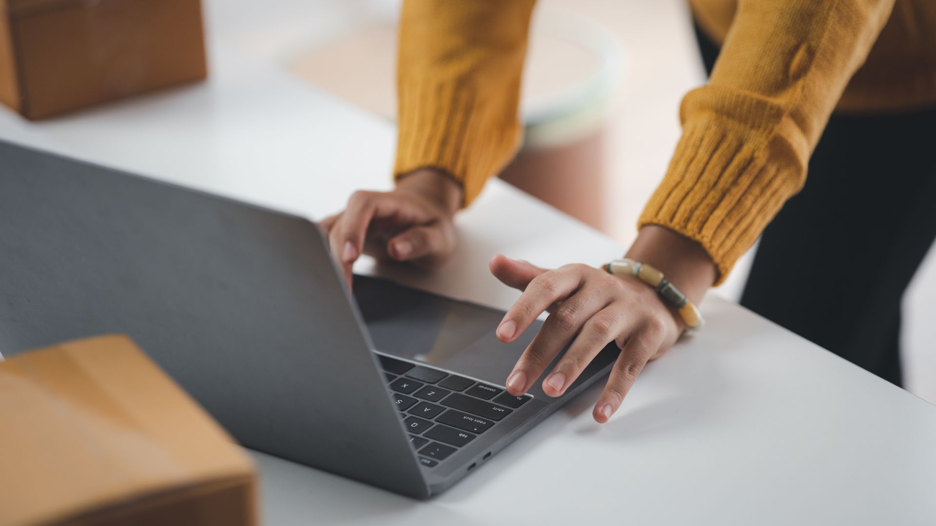 A woman in a yellow sweater is typing on a laptop computer.