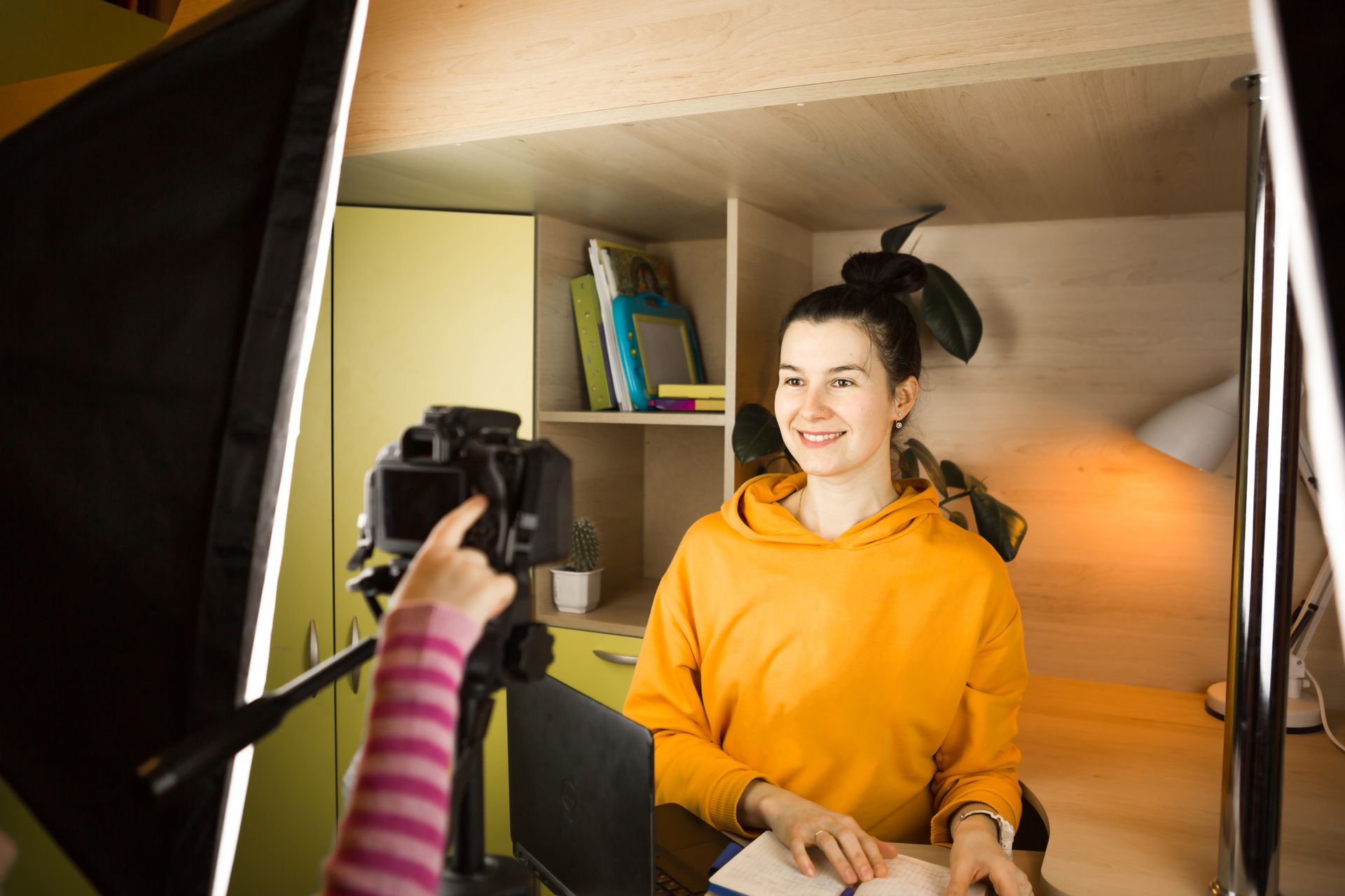 A person is taking a picture of a woman in a yellow hoodie.