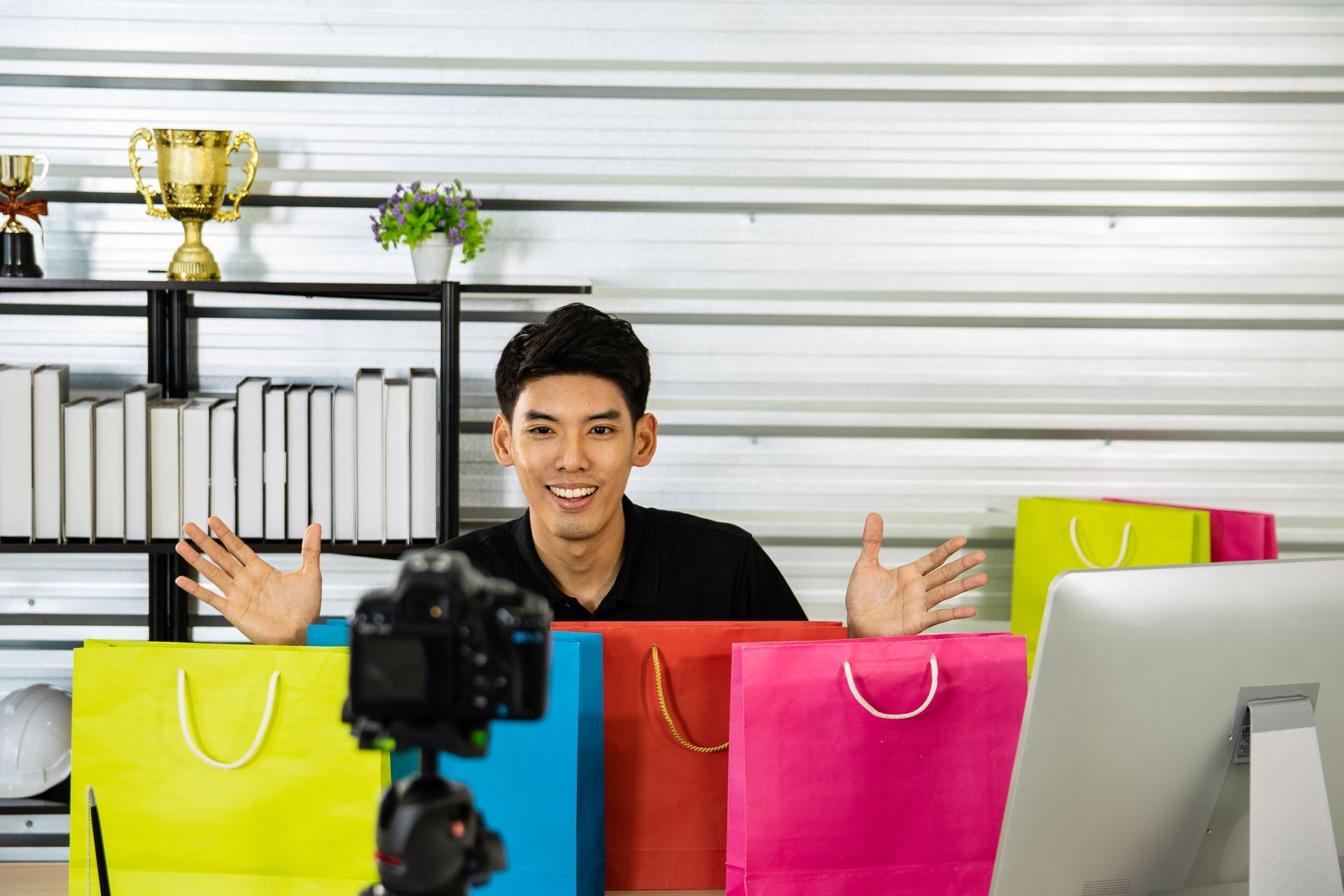 A man is sitting at a desk with shopping bags and a computer.