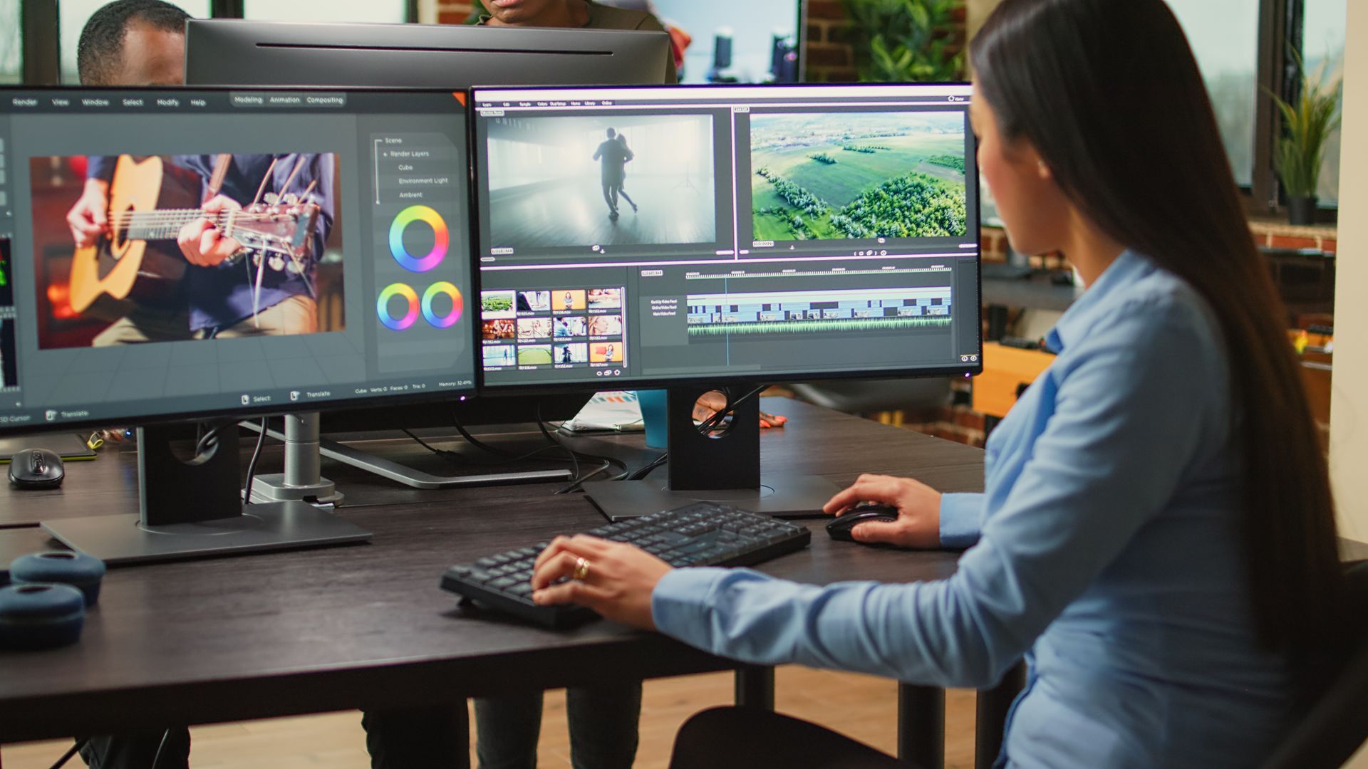 A woman is sitting at a desk in front of two computer monitors.