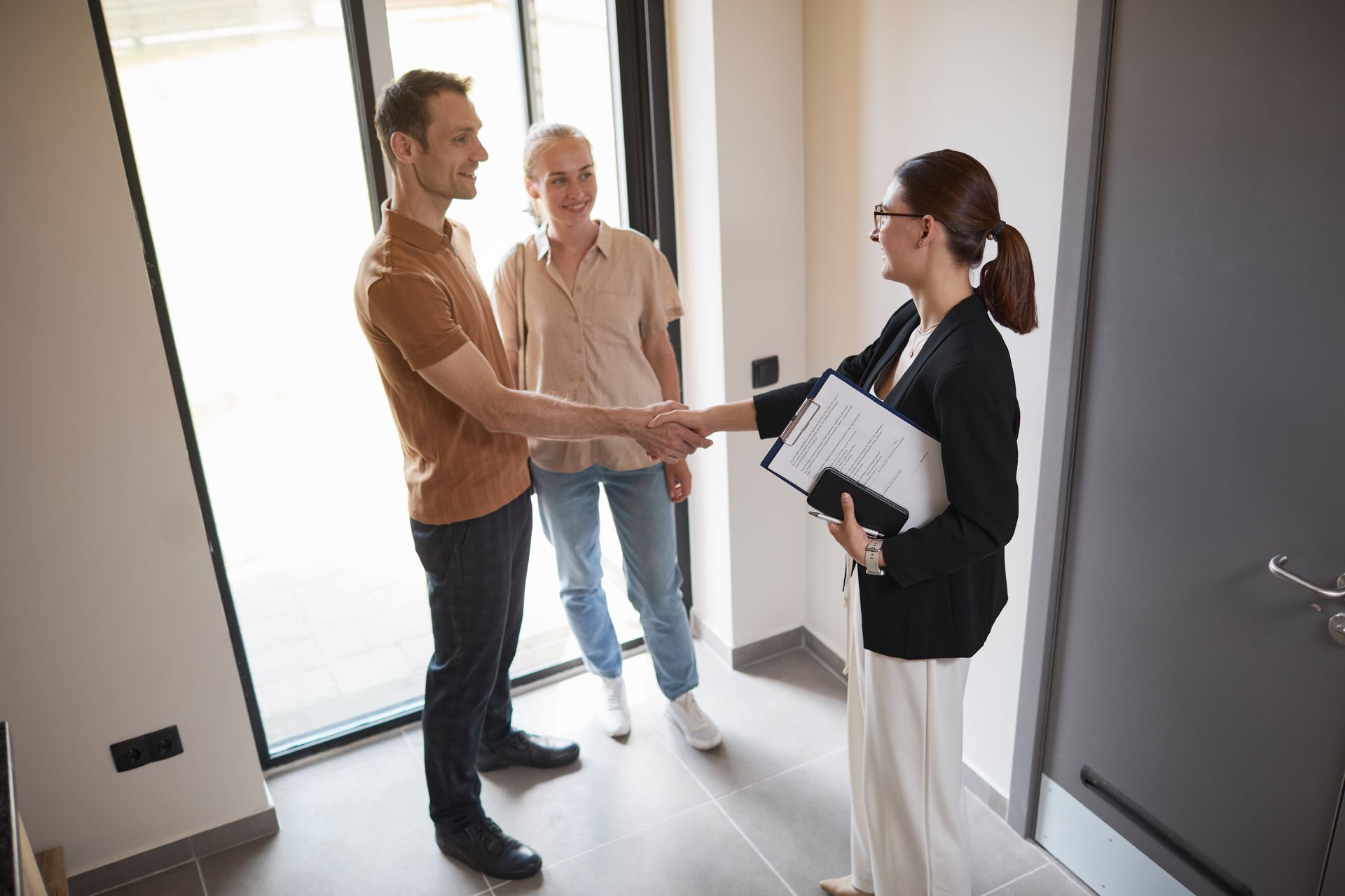 A man and woman are shaking hands with a real estate agent in a hallway.